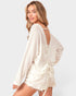 Woman wearing a cream-colored open-back top and shorts on a white background