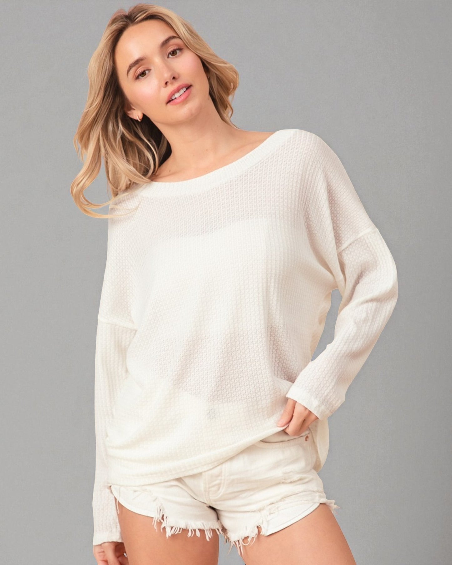 Woman wearing a white sweater and shorts against a gray background