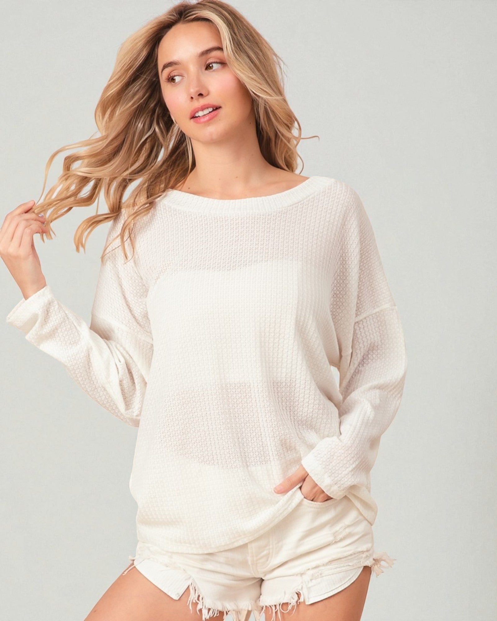 Woman wearing a white sweater and shorts against a plain background