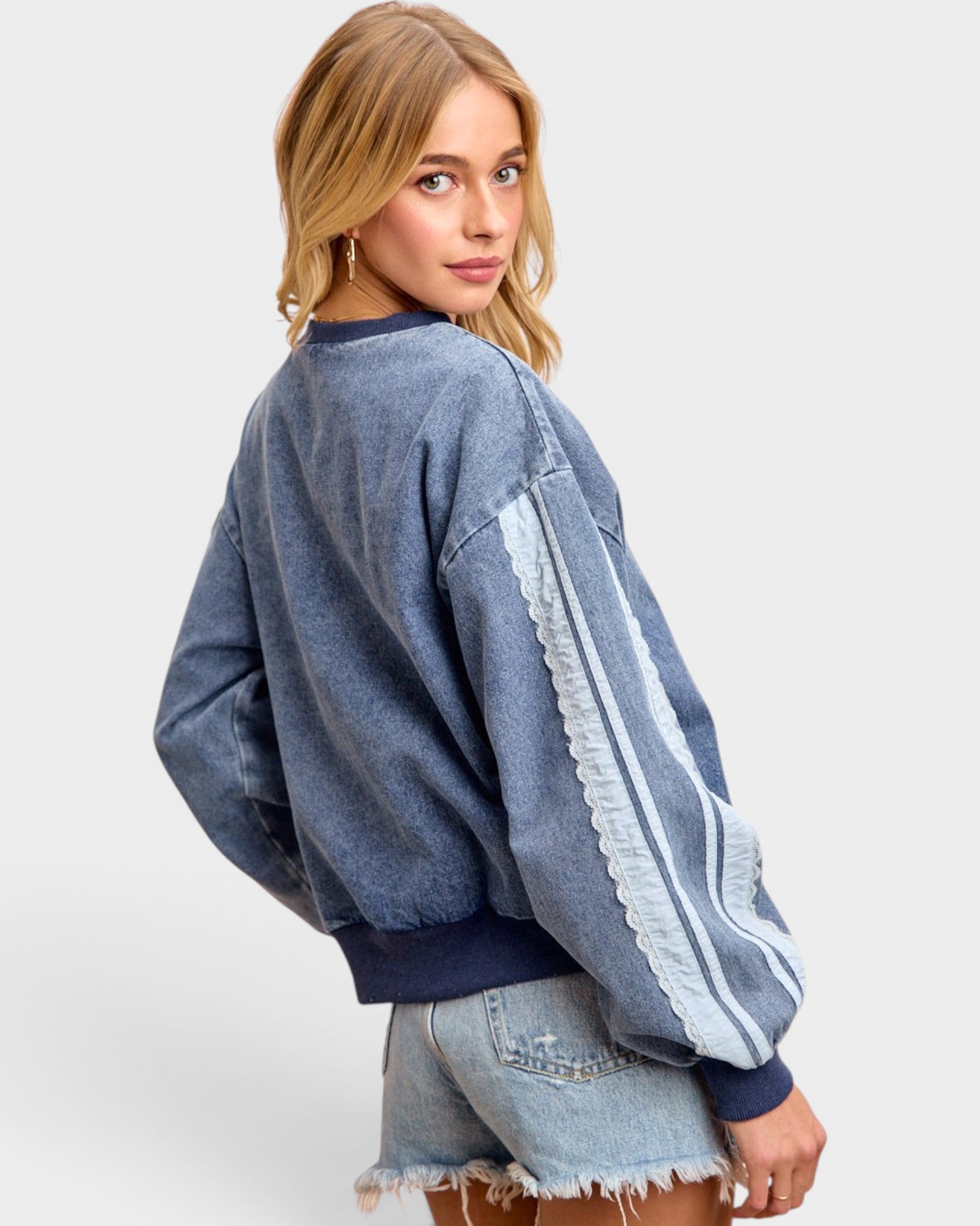 Woman wearing a blue denim jacket with white stripes on a plain background