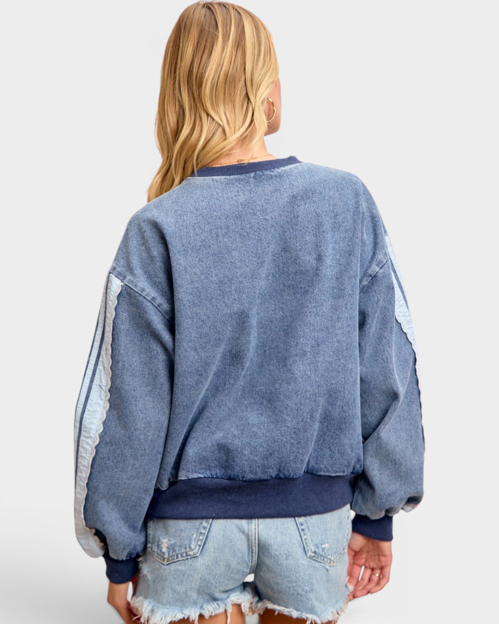 Person wearing a blue distressed sweatshirt and denim shorts on a white background
