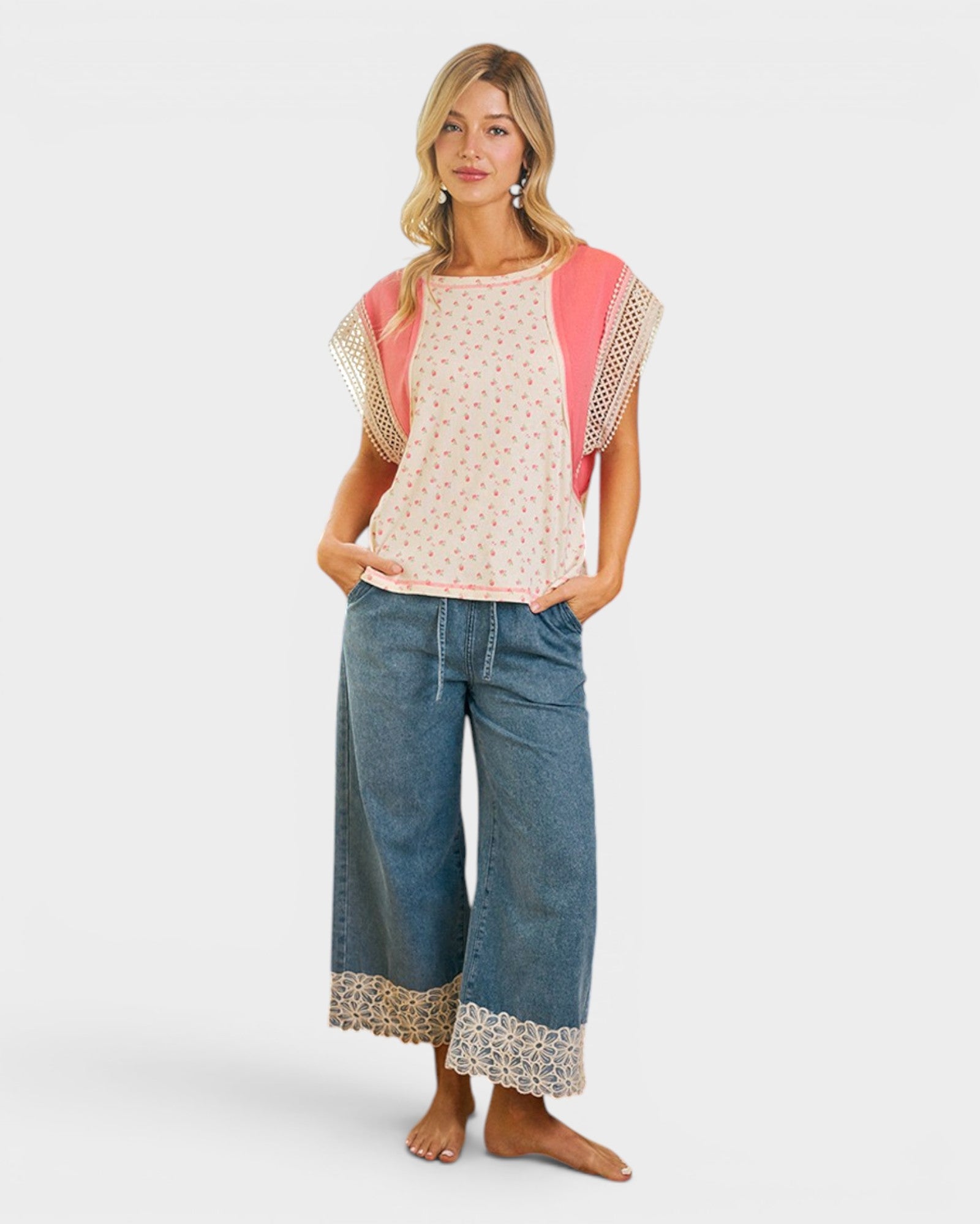 Woman wearing a pink top with floral sleeves and blue jeans on a white background