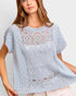 Woman wearing a light blue crochet top against a plain background