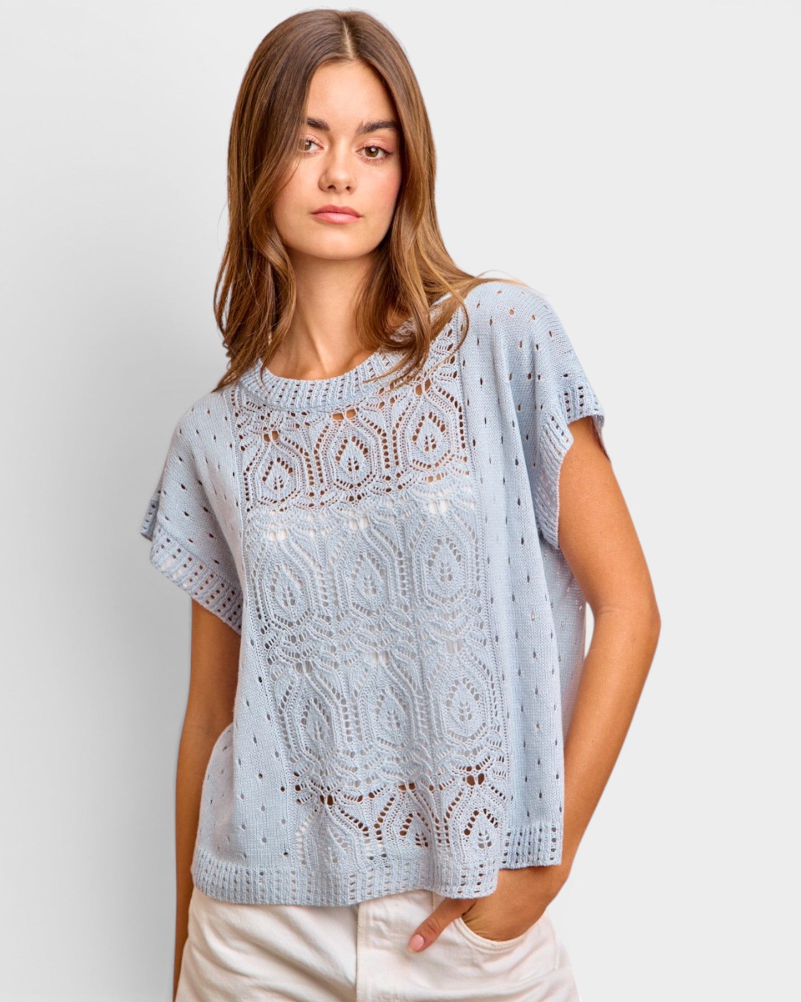 Woman wearing a light blue crochet top against a plain background