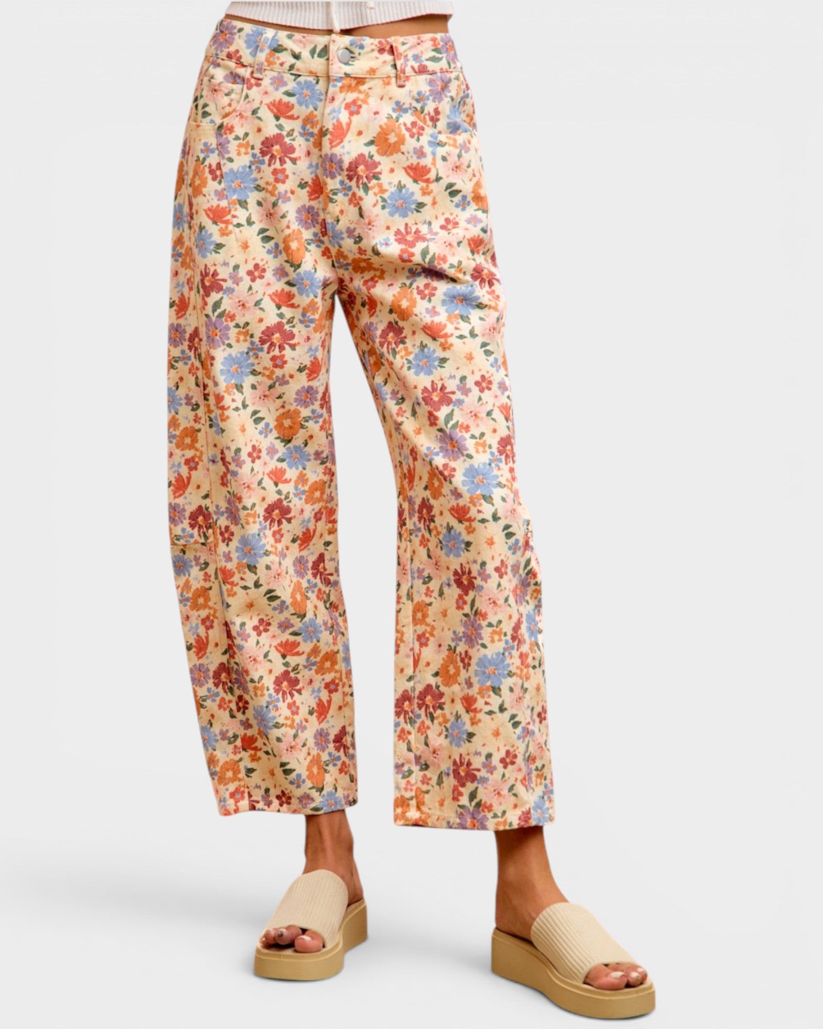 A person wearing cropped wide-leg floral pants with a cream base and multicolor flowers, paired with beige slide sandals, against a light gray studio background.
