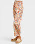 A person shown from the waist down wearing floral cropped pants with a beige base and multicolor flowers, paired with beige slide sandals, against a light gray studio background.