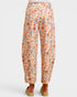 A pair of wide-leg cropped pants with an all-over colorful floral print on a light cream background, shown from the back on a model wearing tan platform sandals against a light gray studio background.