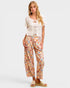A woman modeling a two-piece outfit consisting of a white short-sleeve lace-trim crop top and beige wide-leg pants with a colorful floral print, paired with beige slide sandals against a light gray background.
