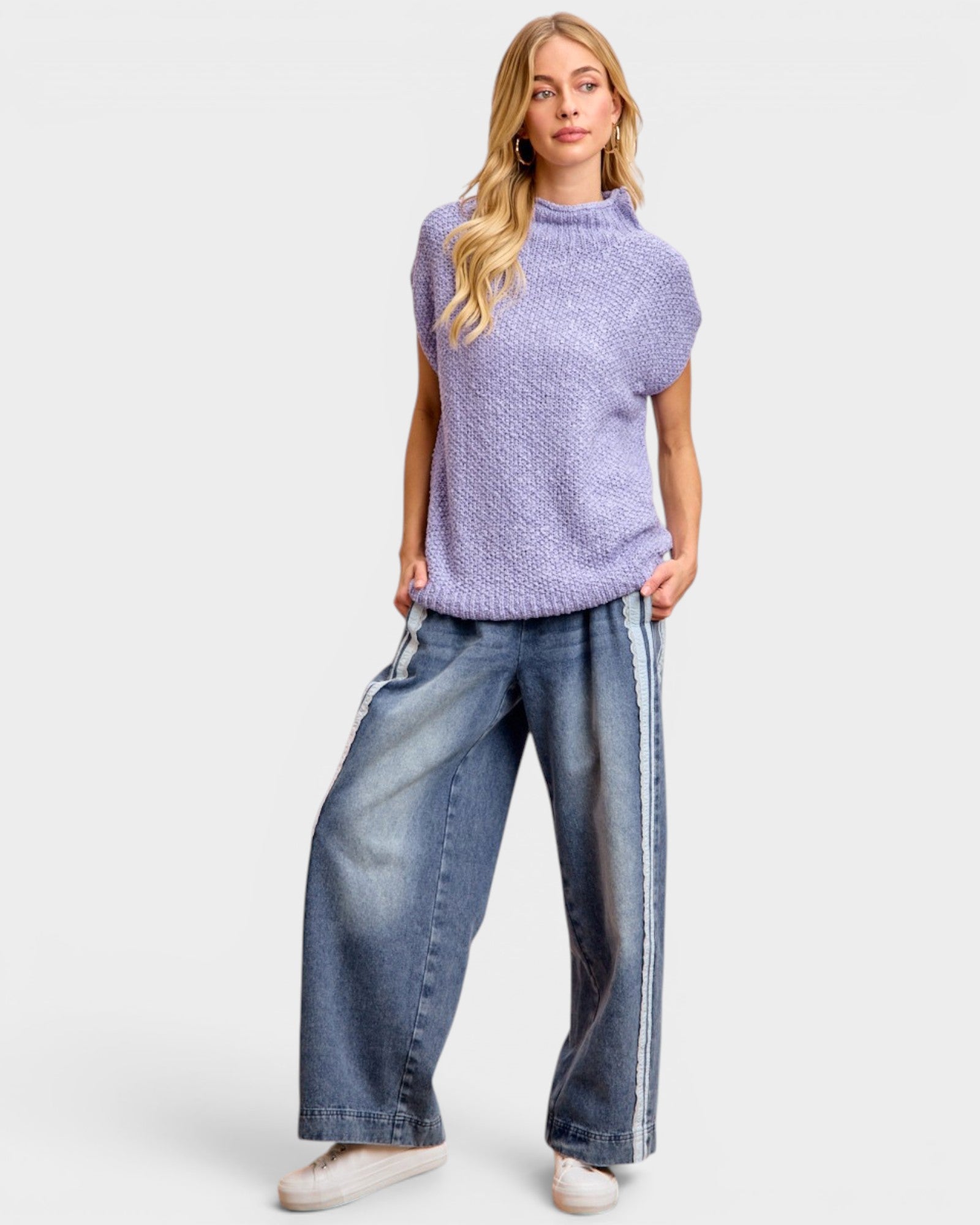 Woman wearing a light purple sleeveless knitted top and blue jeans on a white background