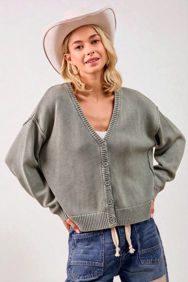 Woman wearing a green cardigan, blue jeans, and a beige hat on a white background