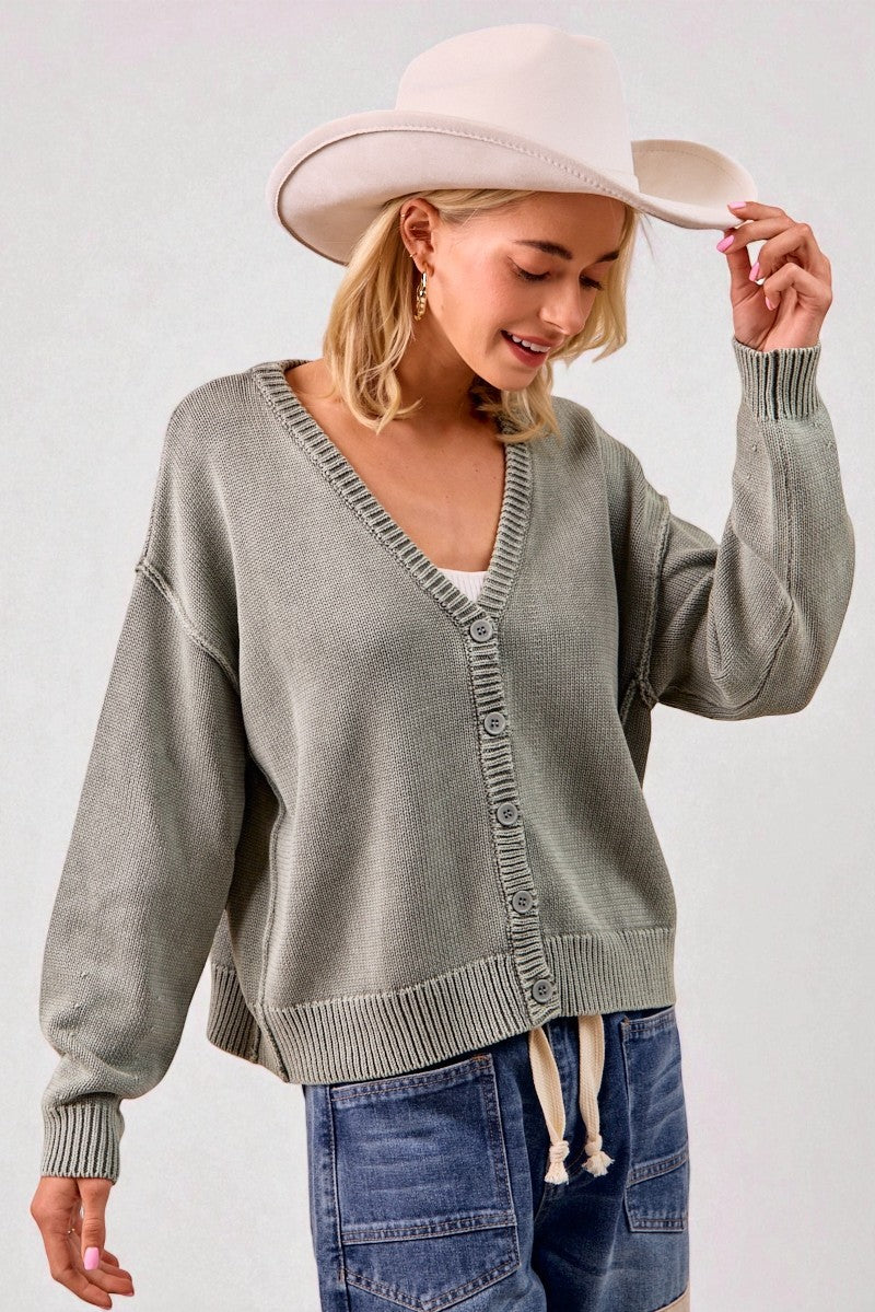 Woman wearing a gray cardigan, blue jeans, and a beige hat against a white background