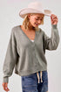 Woman wearing a gray cardigan, blue jeans, and a beige hat against a white background