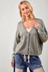 Woman wearing a gray cardigan over a white top with blue shorts on a plain background
