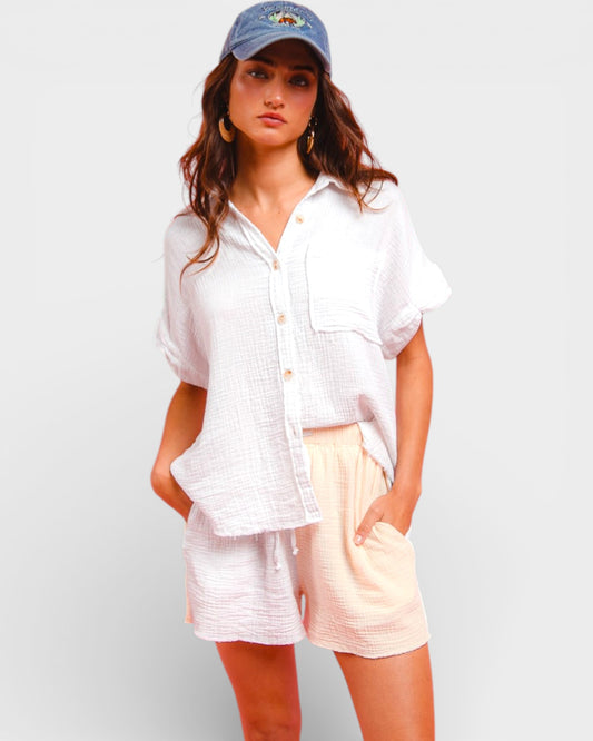 Woman wearing a white shirt and light-colored shorts with a blue cap on a plain background