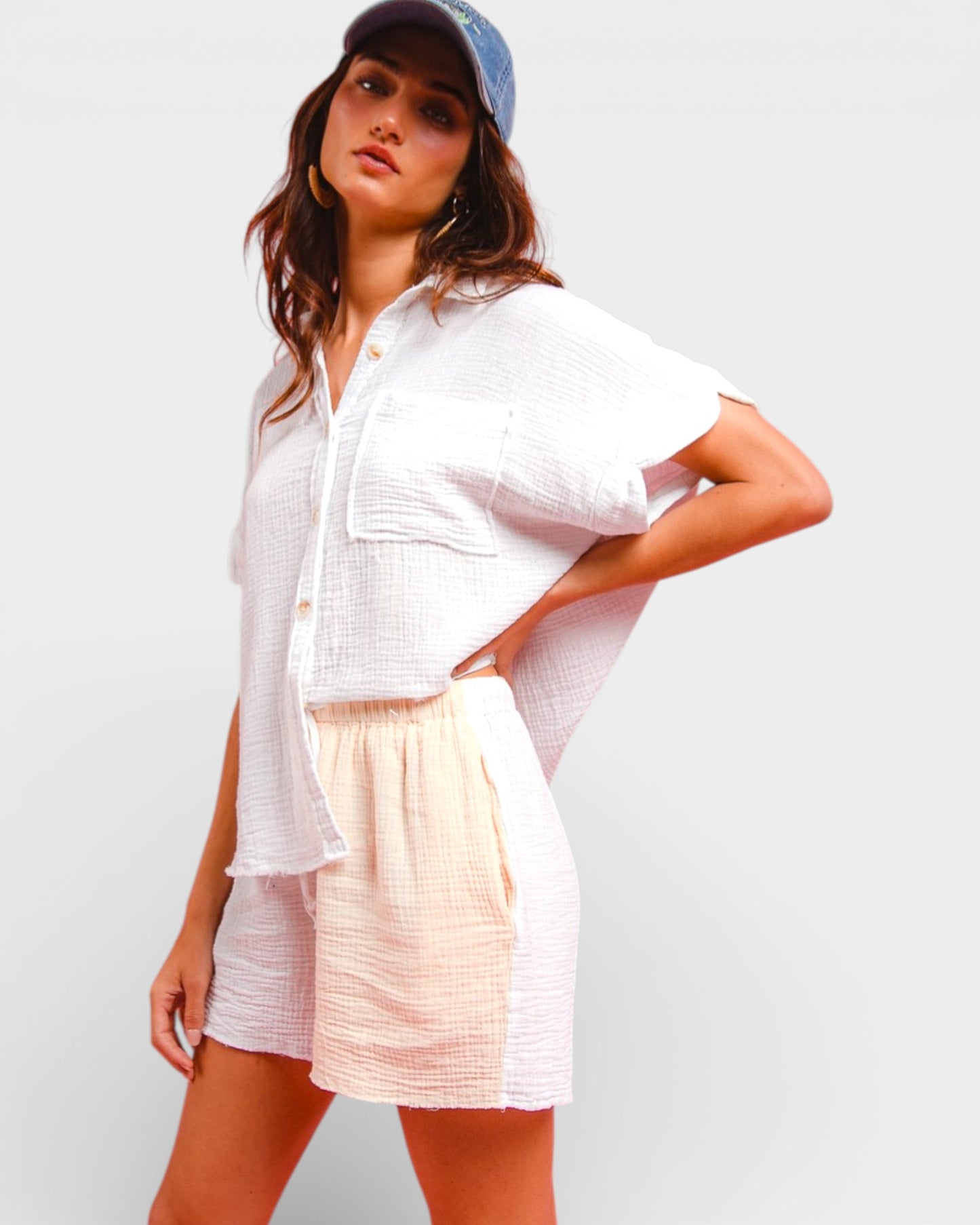 Woman wearing a white shirt and light-colored shorts with a blue cap on a plain background