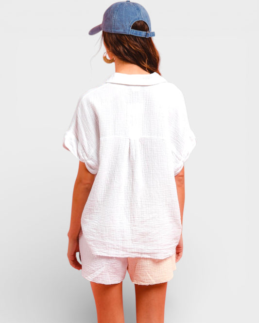 Person wearing a white textured shirt and pink shorts with a blue cap on a plain background