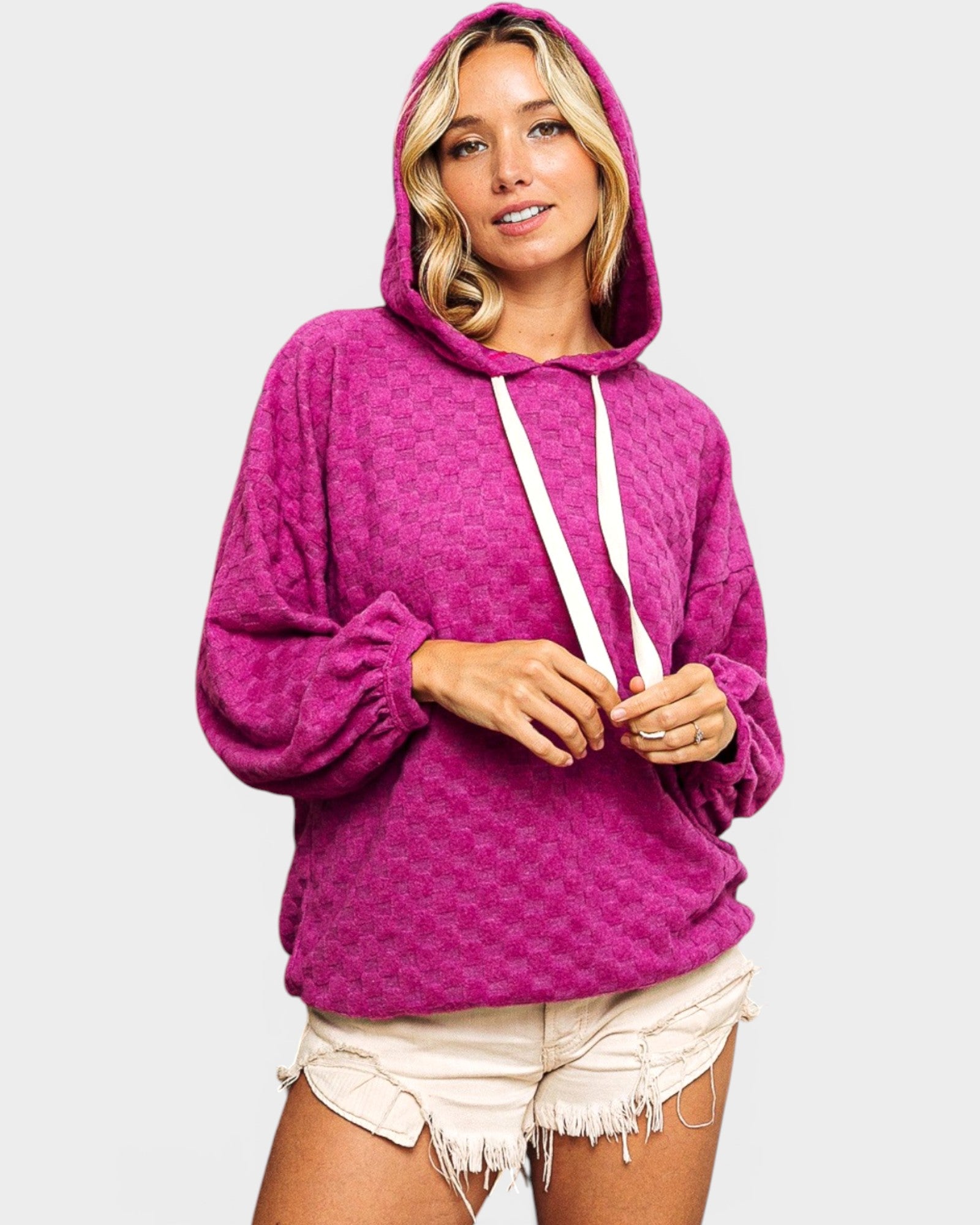 Woman wearing a pink hoodie and white shorts on a light gray background