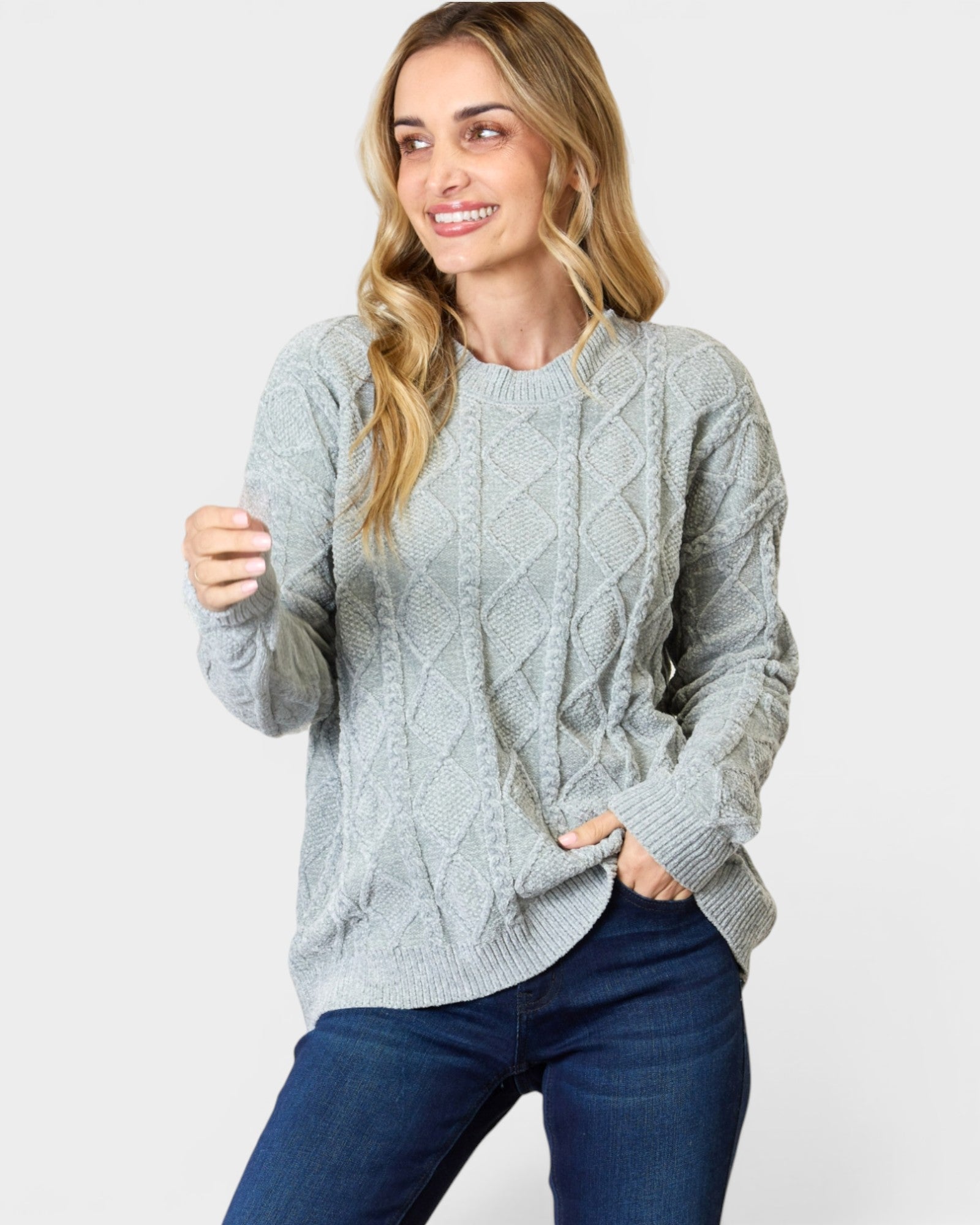 Woman wearing a gray cable knit sweater and blue jeans on a light gray background