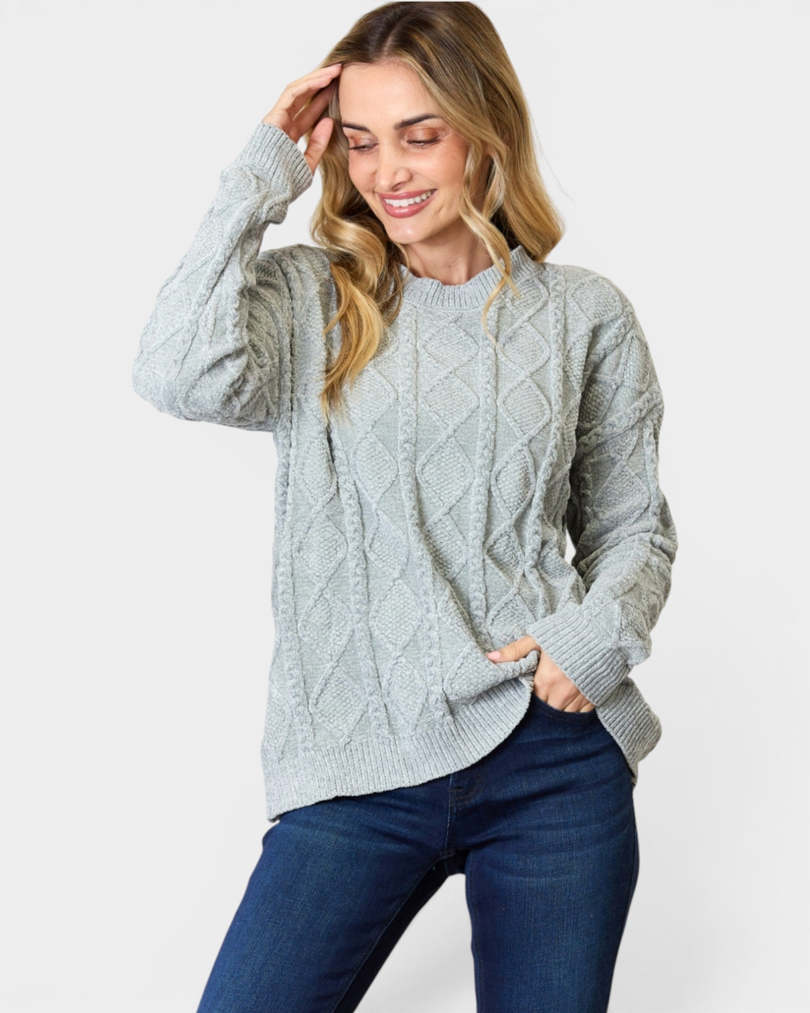 Woman wearing a light gray cable knit sweater and blue jeans on a white background