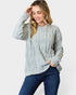Woman wearing a light gray cable knit sweater and blue jeans on a white background