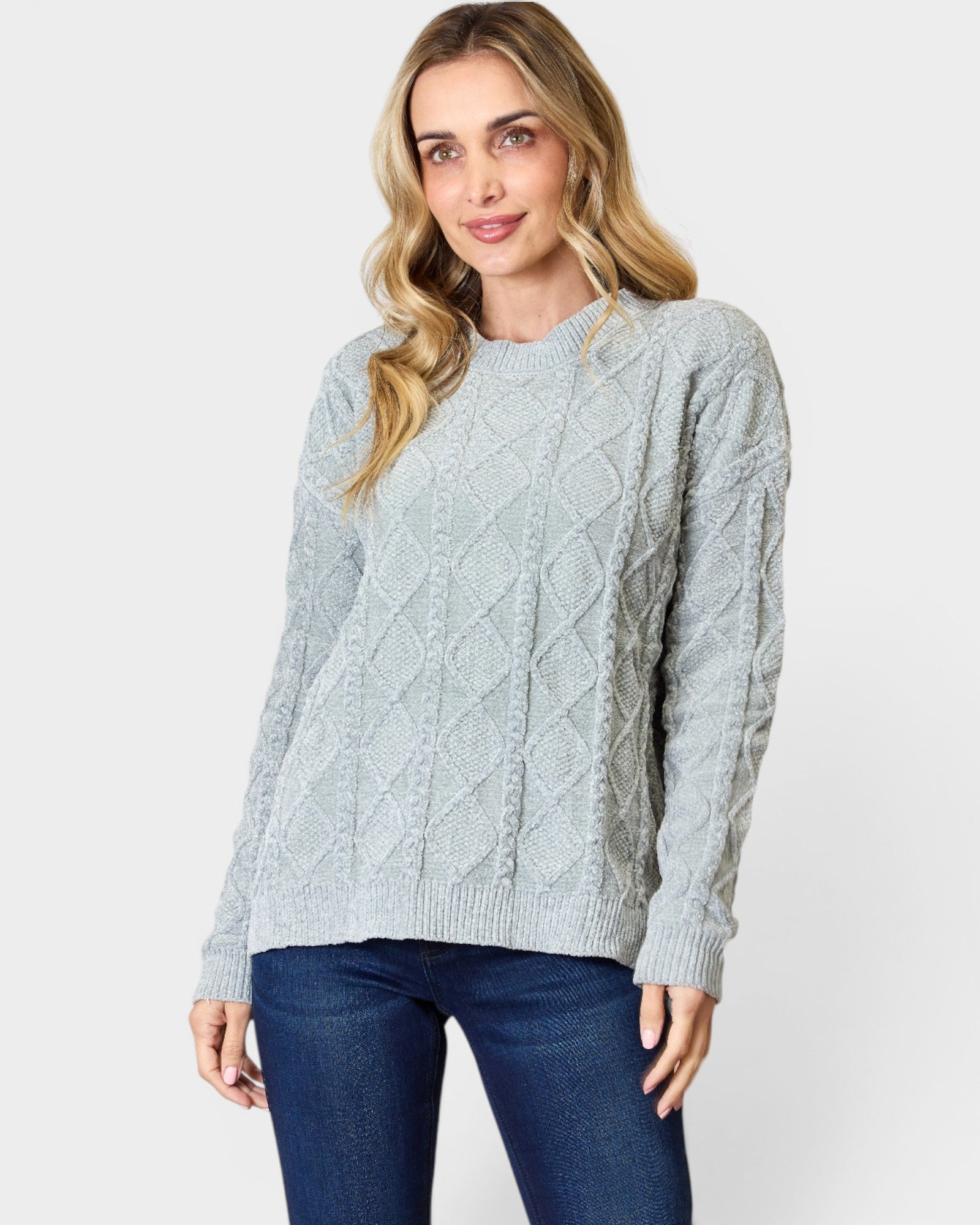 Woman wearing a light blue cable knit sweater and jeans on a white background