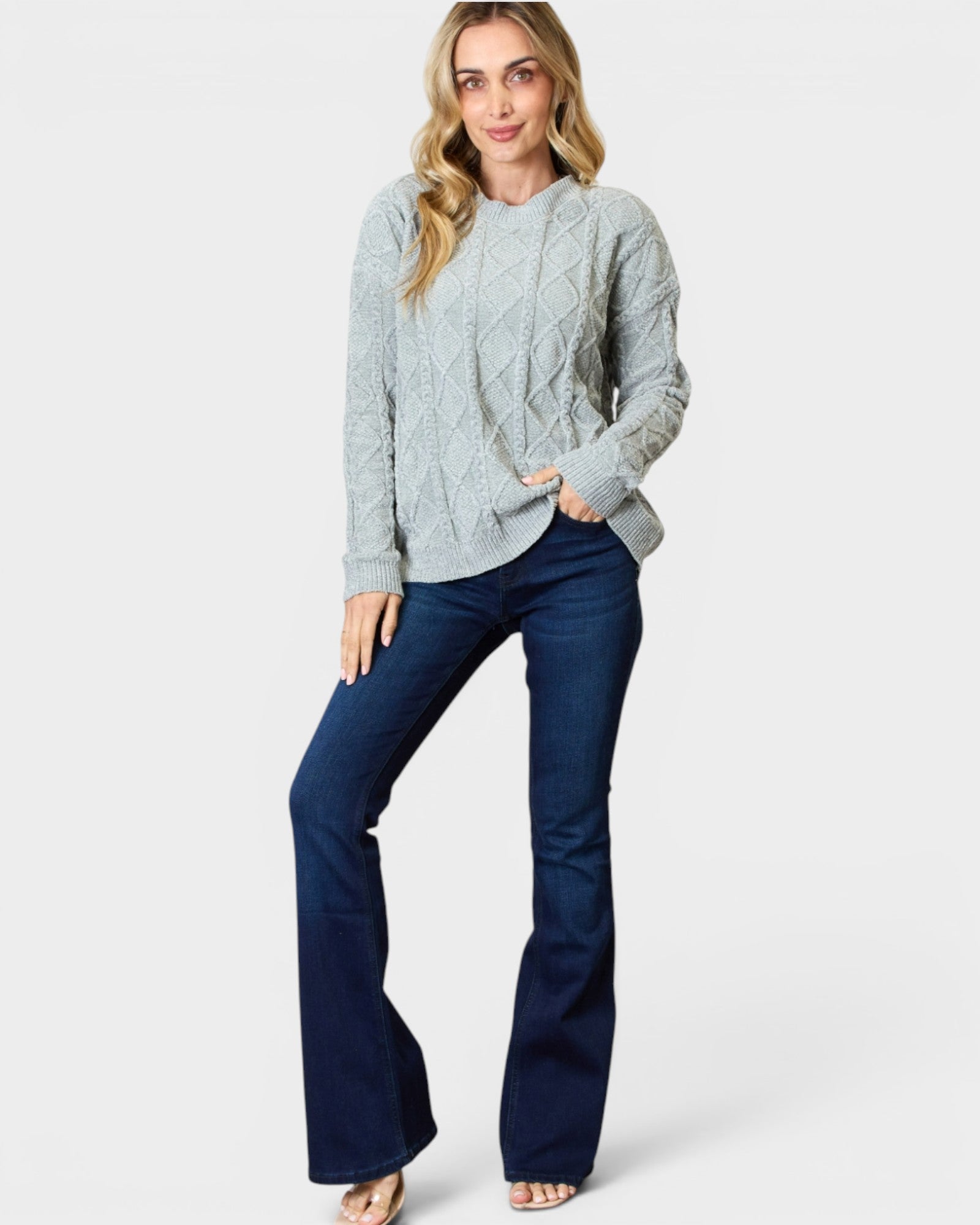 Woman wearing a light gray cable knit sweater and dark blue jeans on a white background