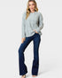 Woman wearing a light gray cable knit sweater and dark blue jeans on a white background
