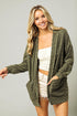 Woman wearing a green cardigan over a white top and shorts on a gray background
