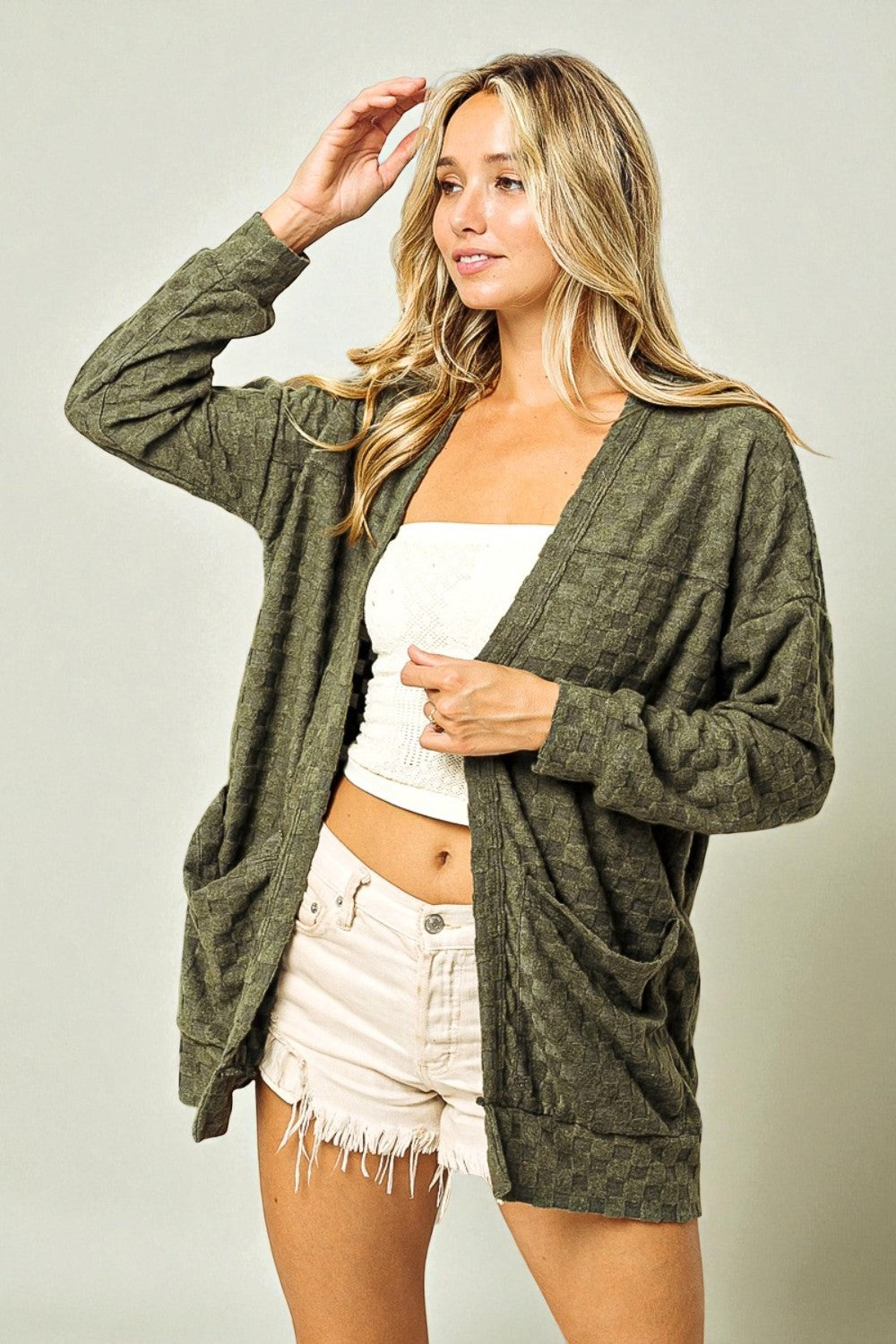 Woman wearing a green cardigan over a white top and shorts on a plain background