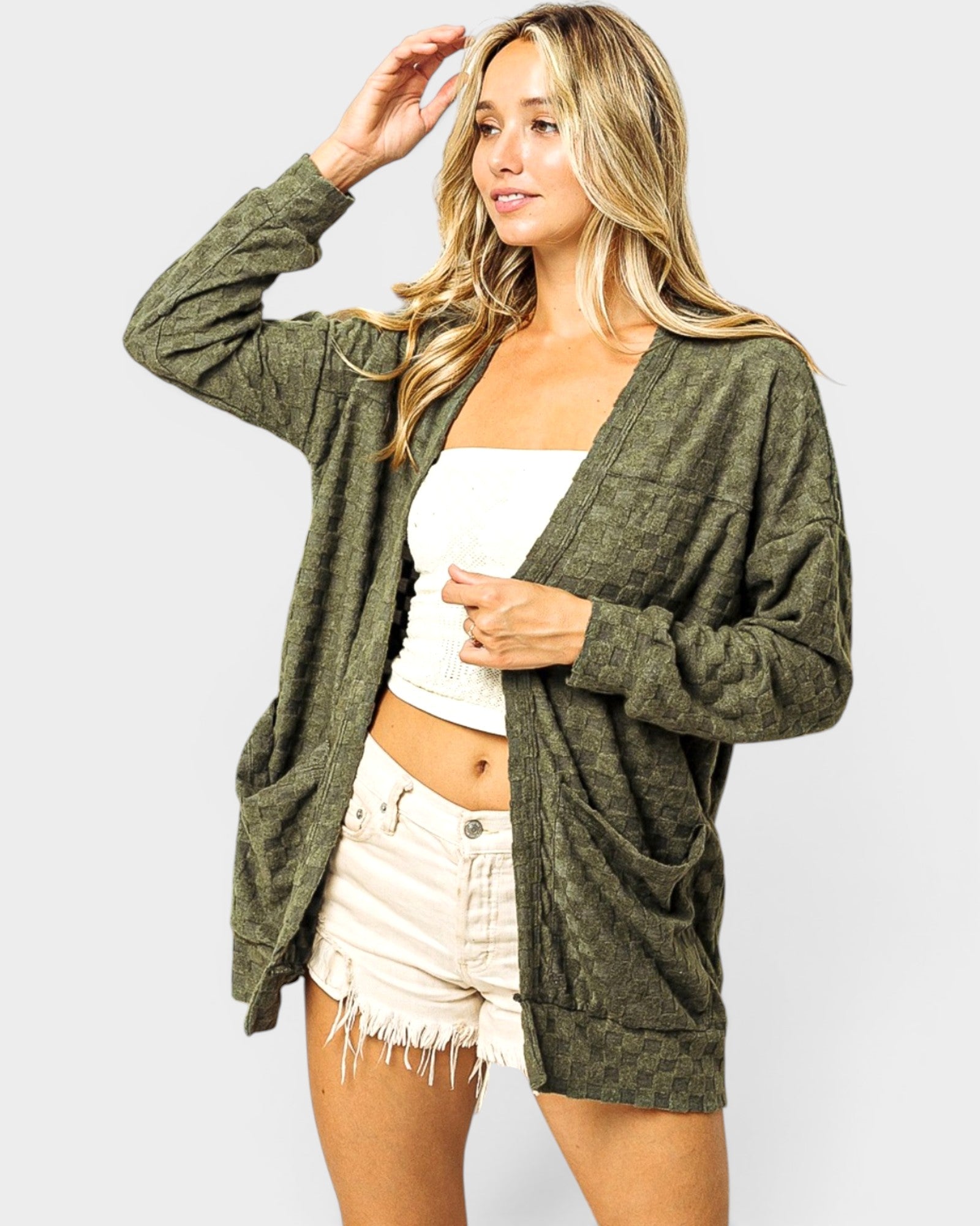 Woman wearing a green cardigan over a white top and beige shorts on a white background