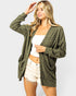 Woman wearing a green cardigan over a white top and beige shorts on a white background