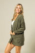 Woman wearing a green cardigan over a white top against a beige background
