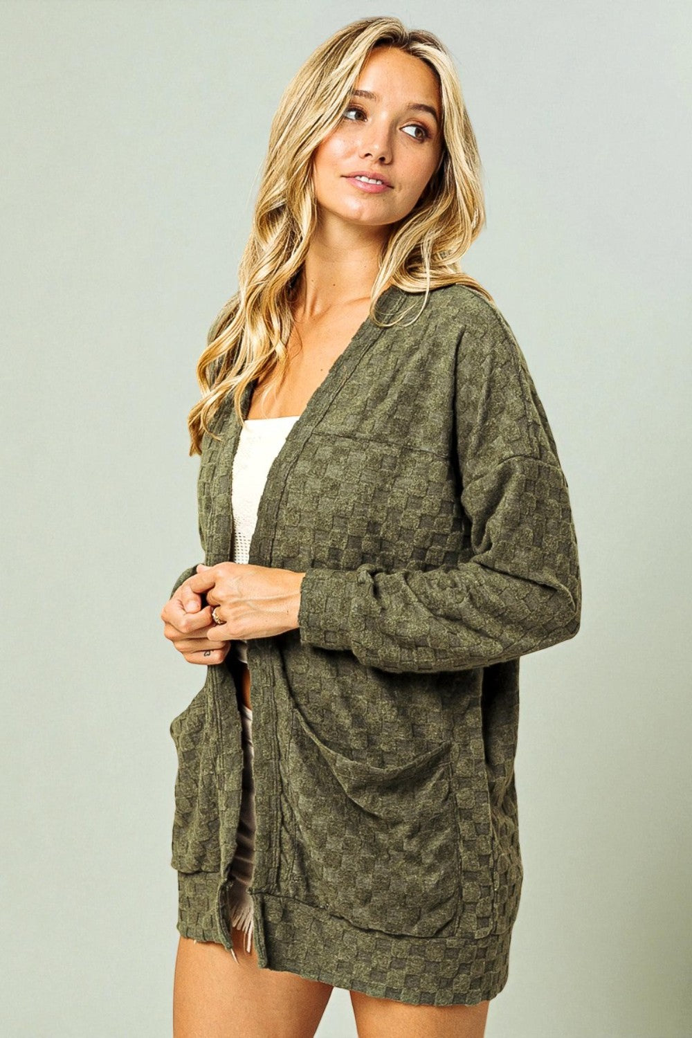 Woman wearing a green cardigan over a white top against a plain background