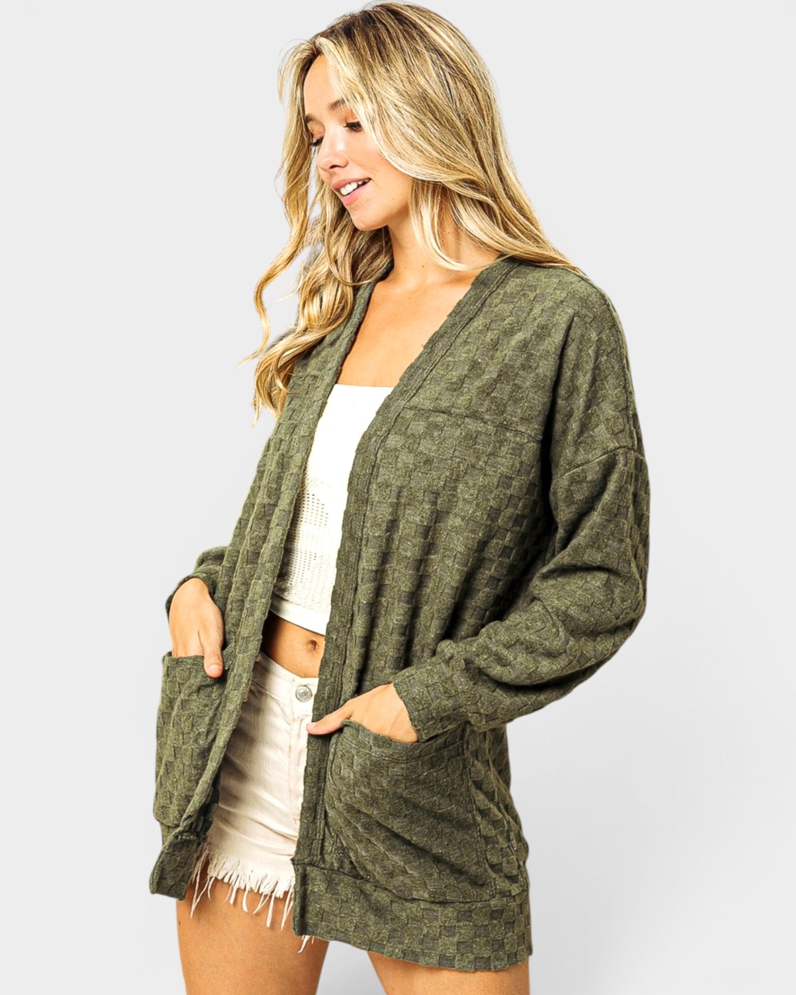Woman wearing a green cardigan over a white top and shorts on a light gray background
