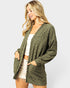 Woman wearing a green cardigan over a white top and shorts on a light gray background