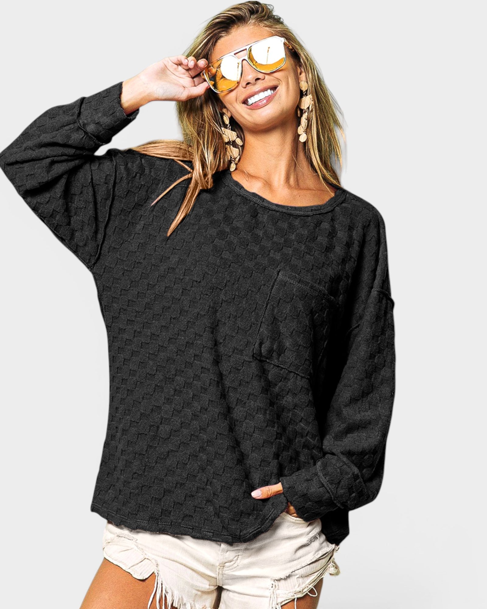 Woman wearing a black long-sleeve top and white shorts with sunglasses on a plain background