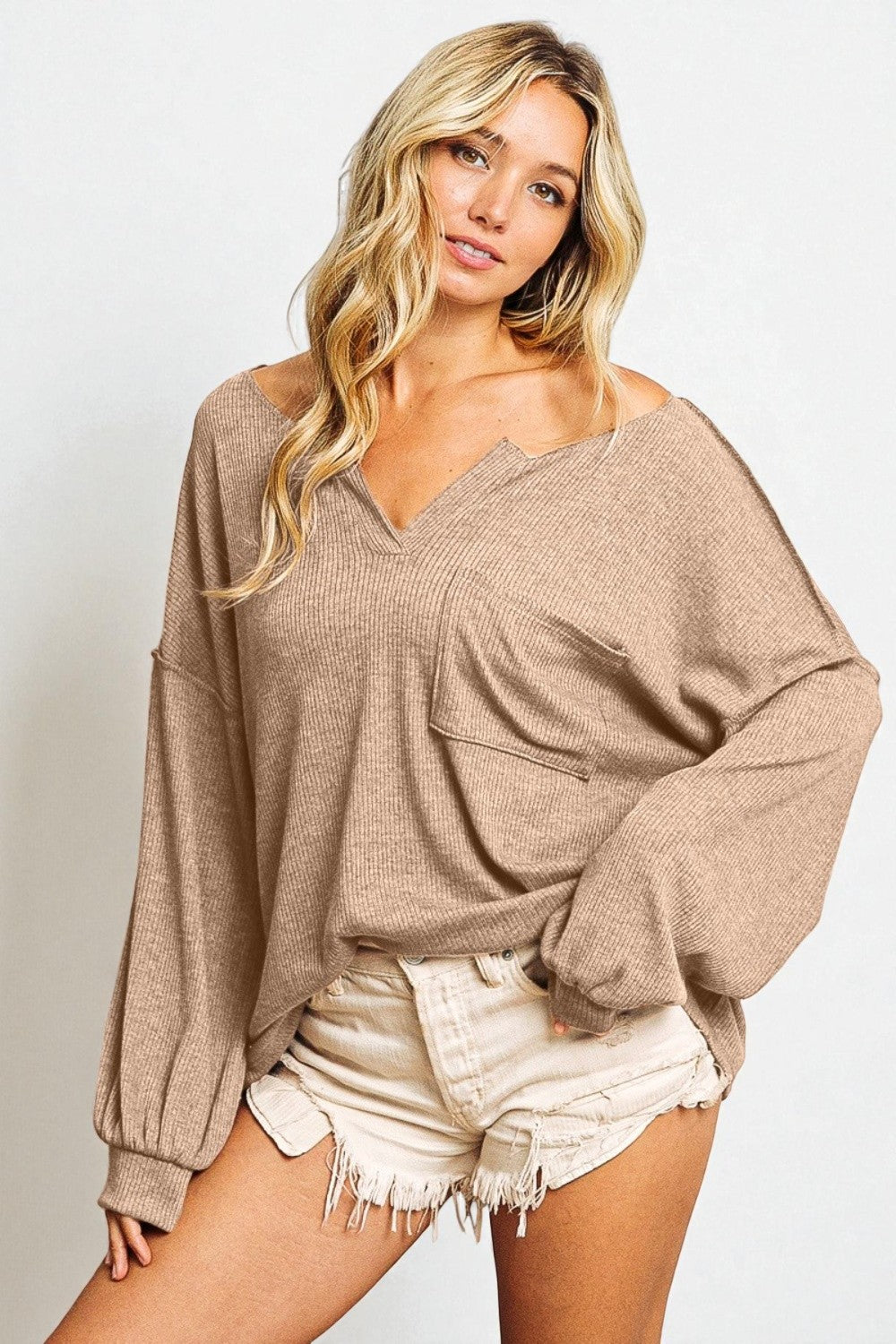 Woman wearing a beige sweater and white shorts on a plain background