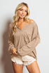 Woman wearing a beige off-shoulder sweater and white shorts on a plain background
