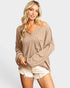 Woman wearing a beige oversized sweater and white shorts on a light gray background