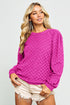Woman wearing a bright pink sweater and white shorts on a light gray background