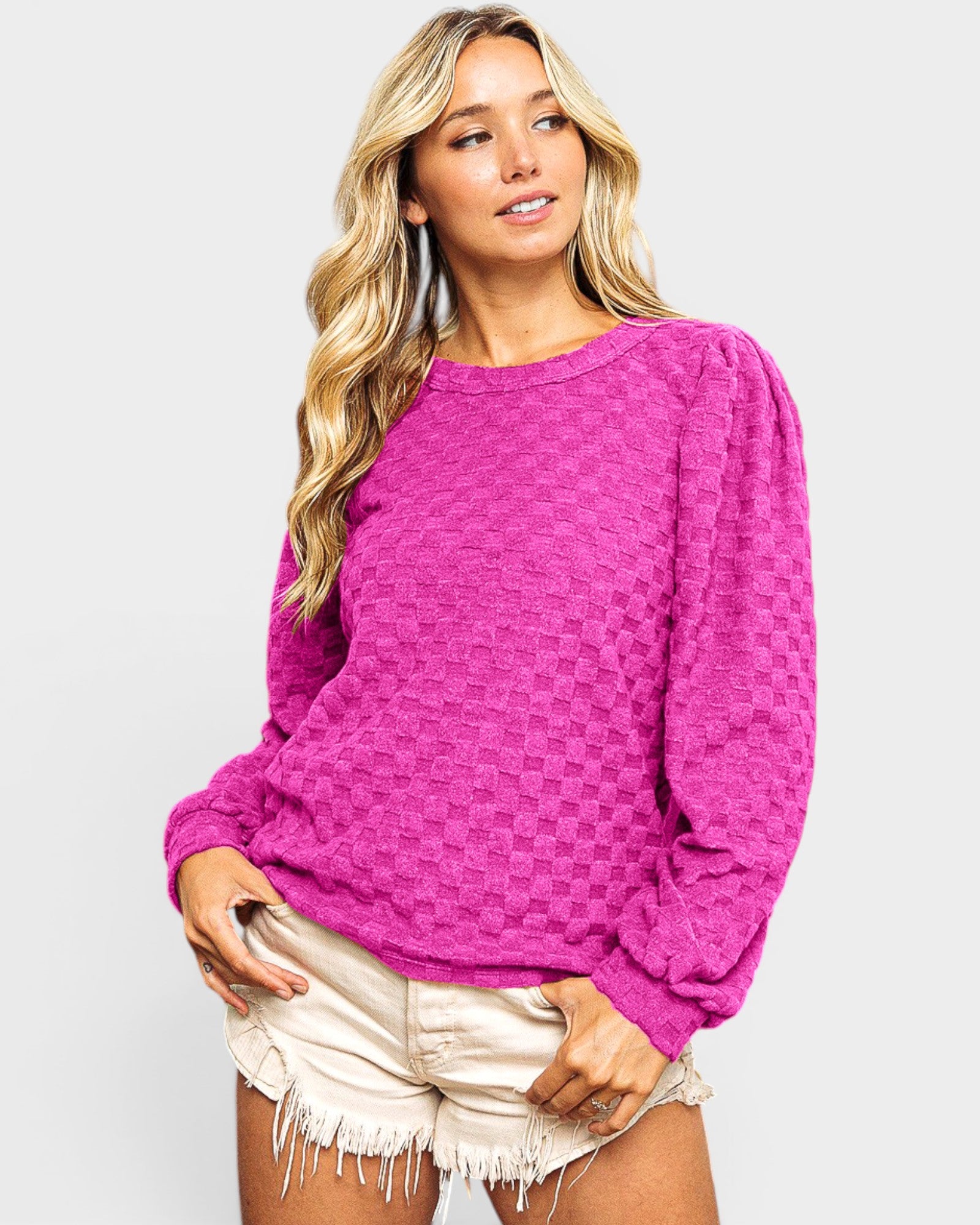Woman wearing a bright pink sweater and white shorts on a light gray background