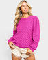Woman wearing a bright pink sweater and white shorts on a light gray background