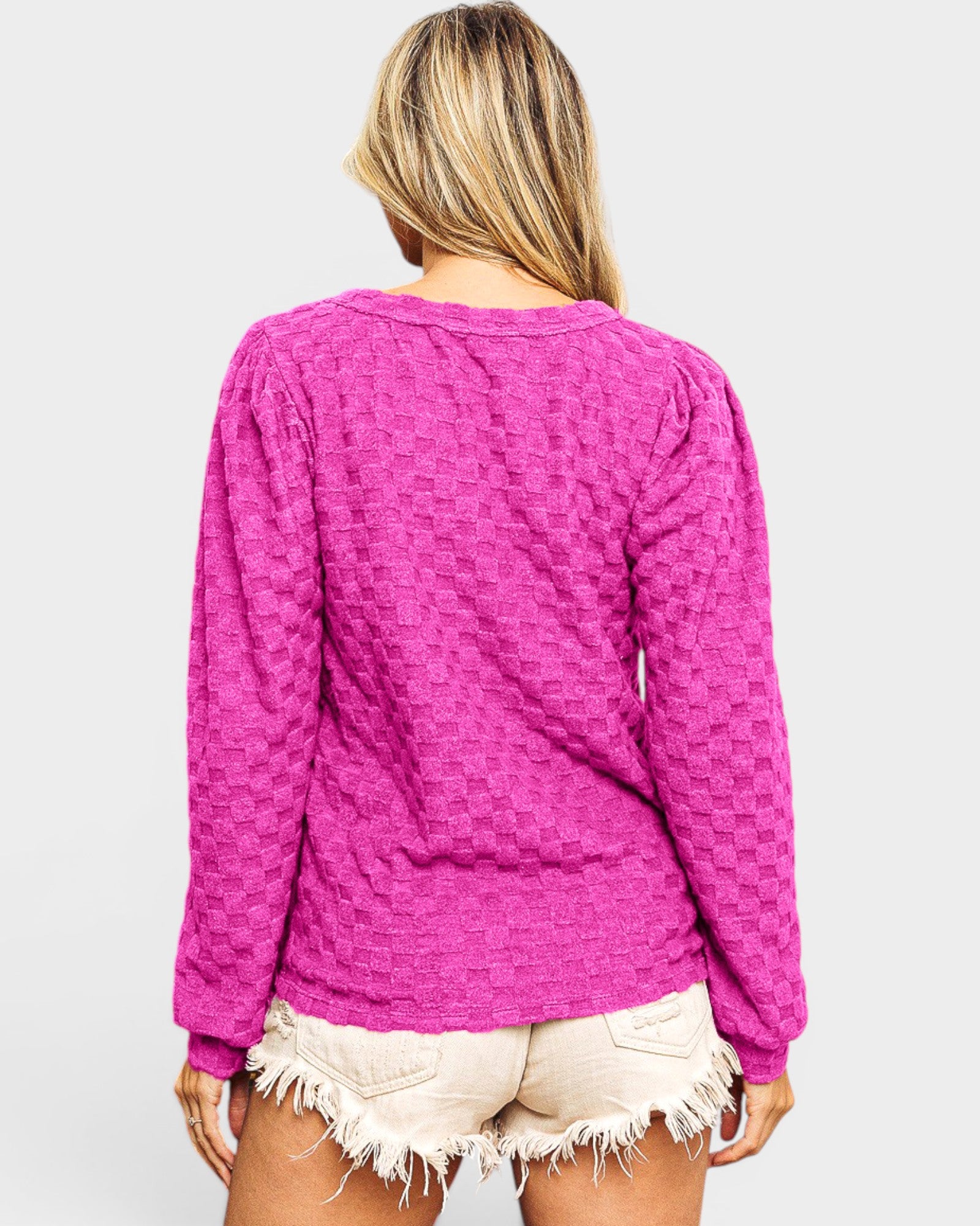 Person wearing a pink textured long-sleeve top and white shorts on a light gray background