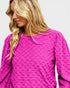 Woman wearing a bright pink textured top against a plain background