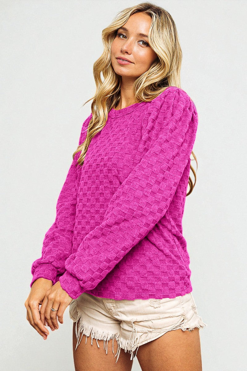 Woman wearing a bright pink textured sweater and white shorts on a light gray background