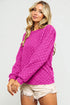Woman wearing a bright pink textured sweater and white shorts on a light gray background