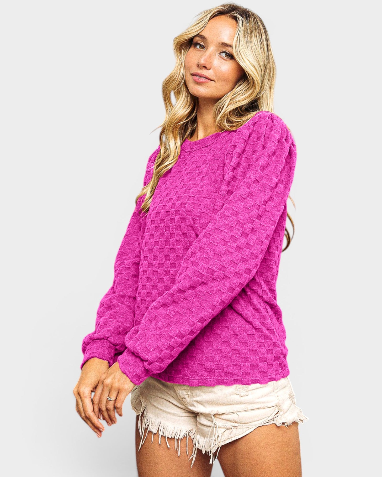 Woman wearing a bright pink textured sweater and white shorts on a light gray background