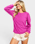 Woman wearing a bright pink textured sweater and white shorts on a light gray background
