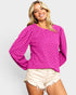 Woman wearing a bright pink textured sweater and white shorts on a light gray background