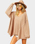 Woman wearing a beige oversized sweater, white shorts, and a wide-brimmed hat on a plain background